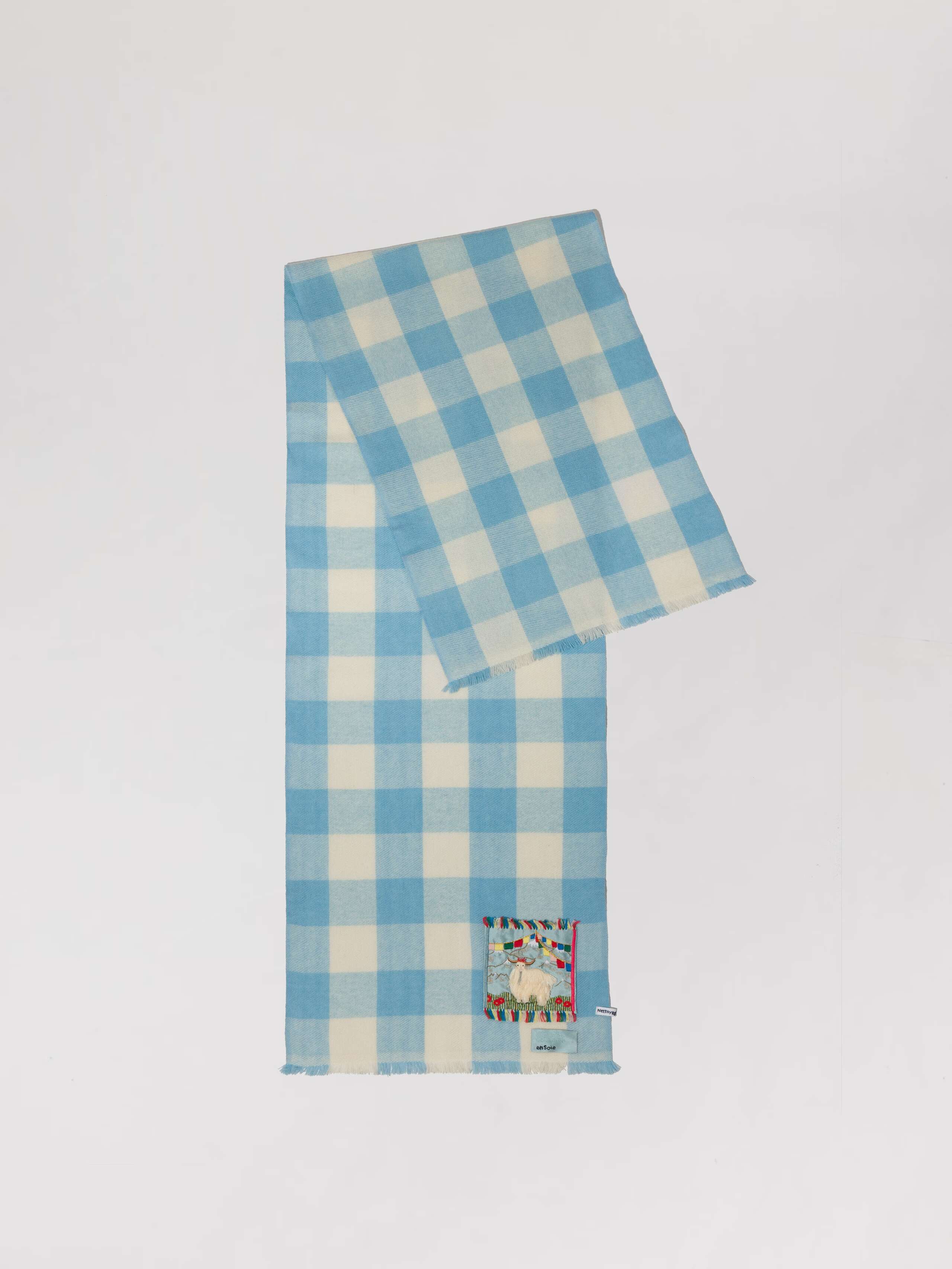 Picture of a detail of a cashmere scarf featuring a light blue and white check pattern